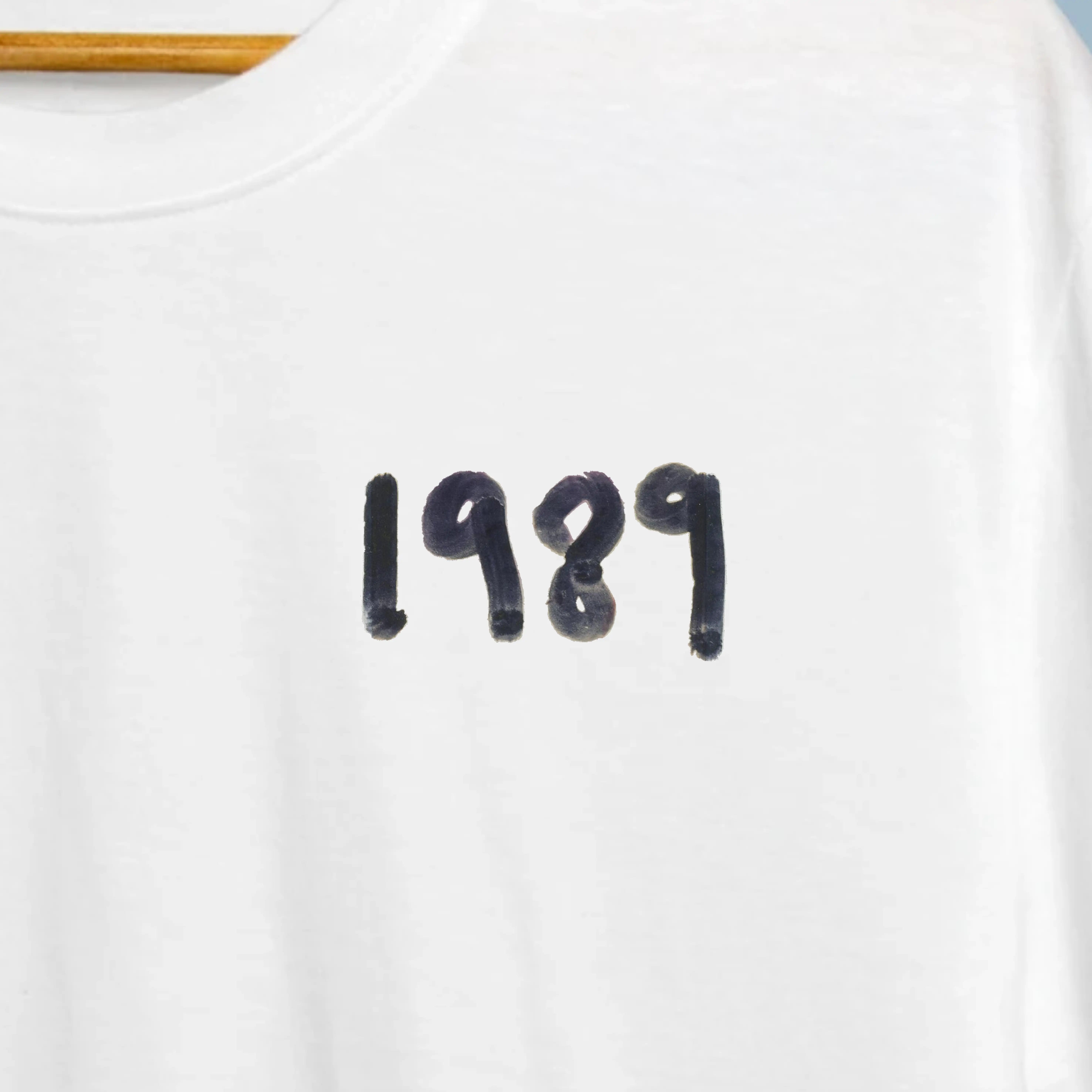 T-Shirt Taylor Swift - 1989 3 Zoom da tipografia 1989 em estilo graffiti azul impressa no peito esquerdo da t-shirt branca